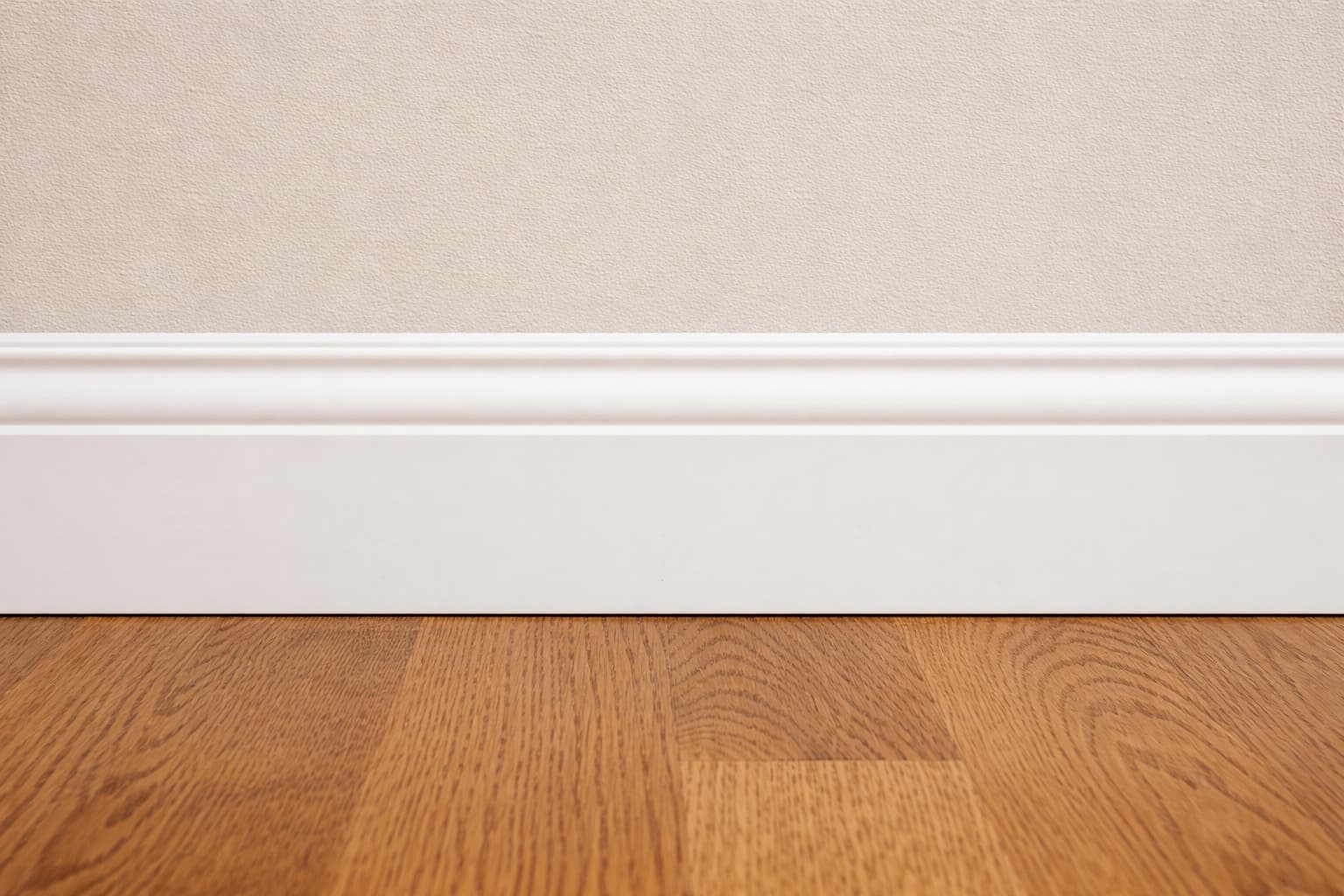 A painted baseboard covers the joint between the wall and wood flooring.